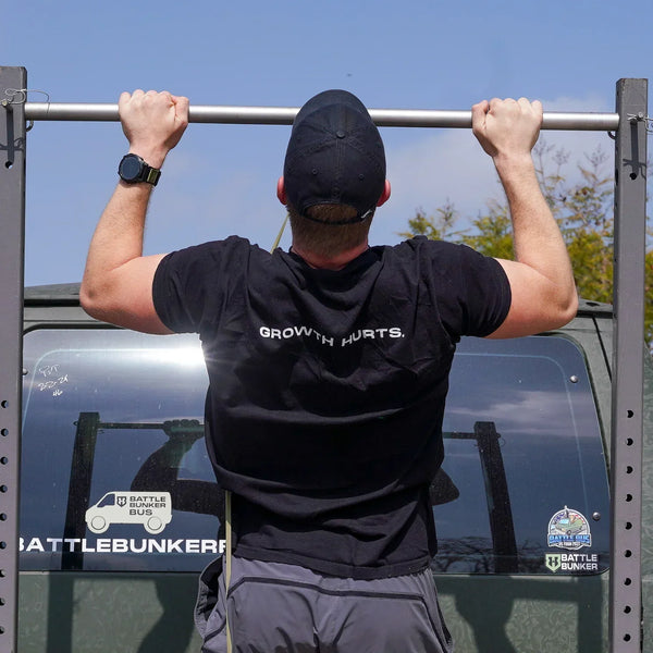 Man in black cap doing pull-ups on battle bunker workout bar outdoors with Battle Bunker Bus decals