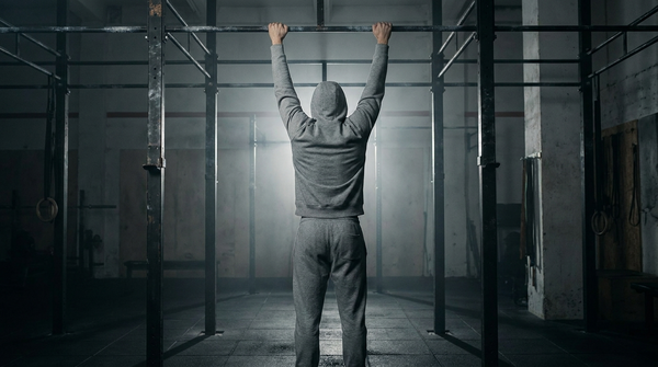 Athlete performing a dead hang from a pull-up bar in a dark gym