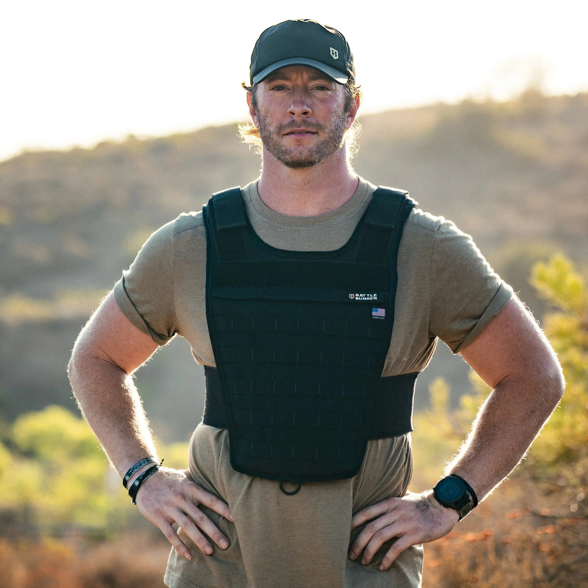 Man outdoors wearing black Battle Bunker tactical vest and cap in natural desert landscape