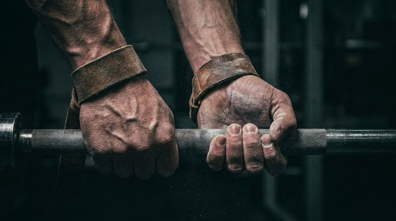 Close-up of hands gripping a barbell with lifting straps