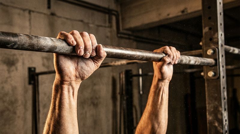Chalked hands gripping a steel pull-up bar