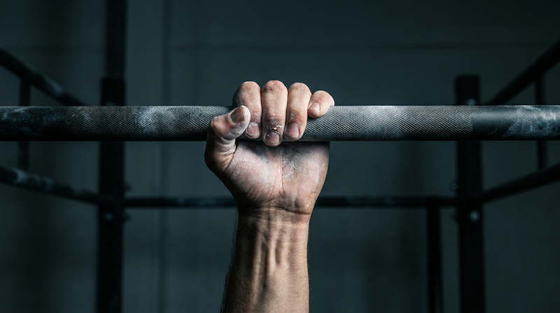 Close-up of a chalked hand gripping a pull-up bar for grip strength training
