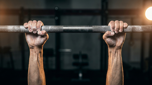 Close-up of chalked hands gripping a pull-up bar during a dead hang