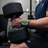 Close-up of muscular arm wearing Battle Wraps wrist support by Battle Bunker holding heavy black dumbbell