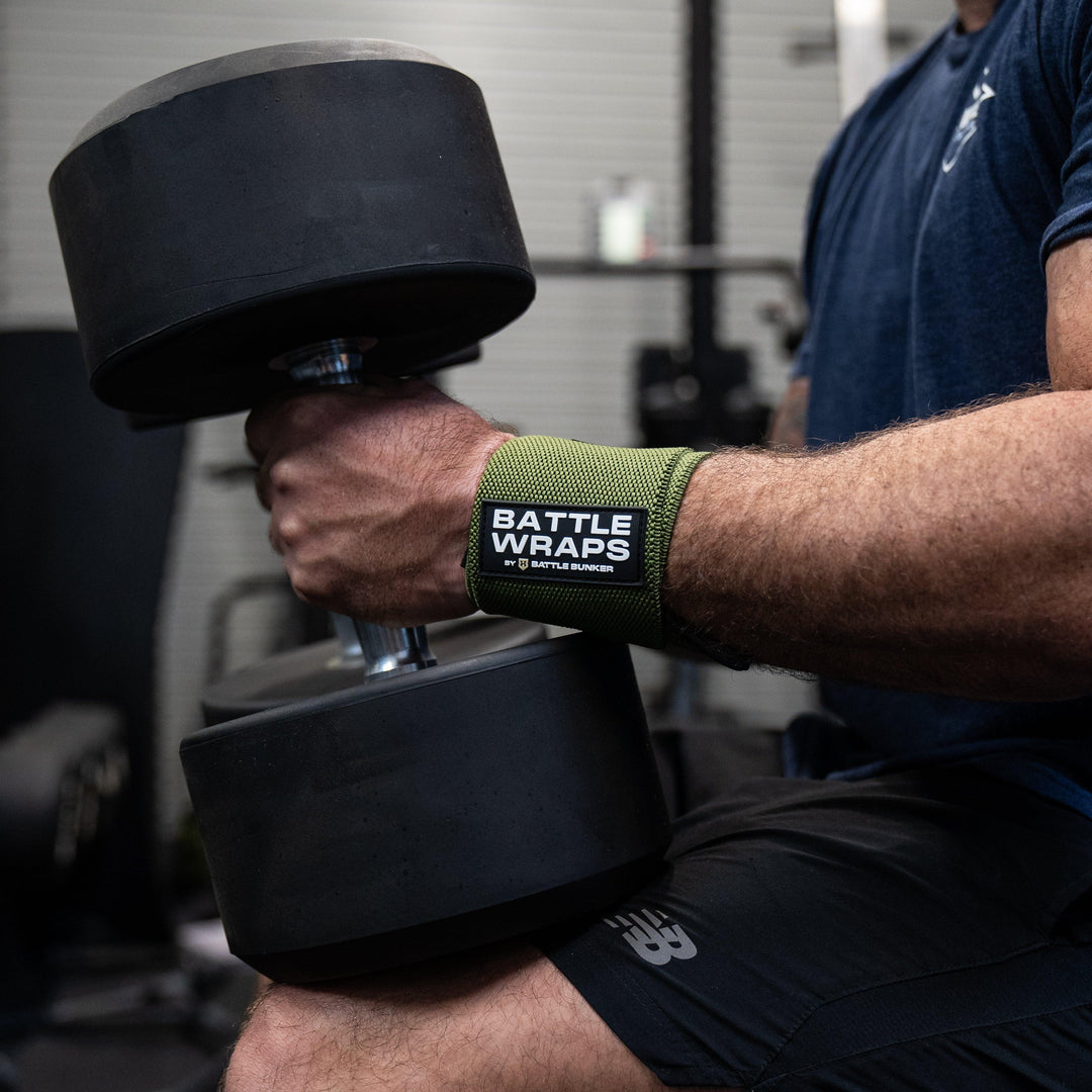 Close-up of muscular arm lifting black dumbbell wearing green Battle Wraps wrist wraps by Battle Bunker