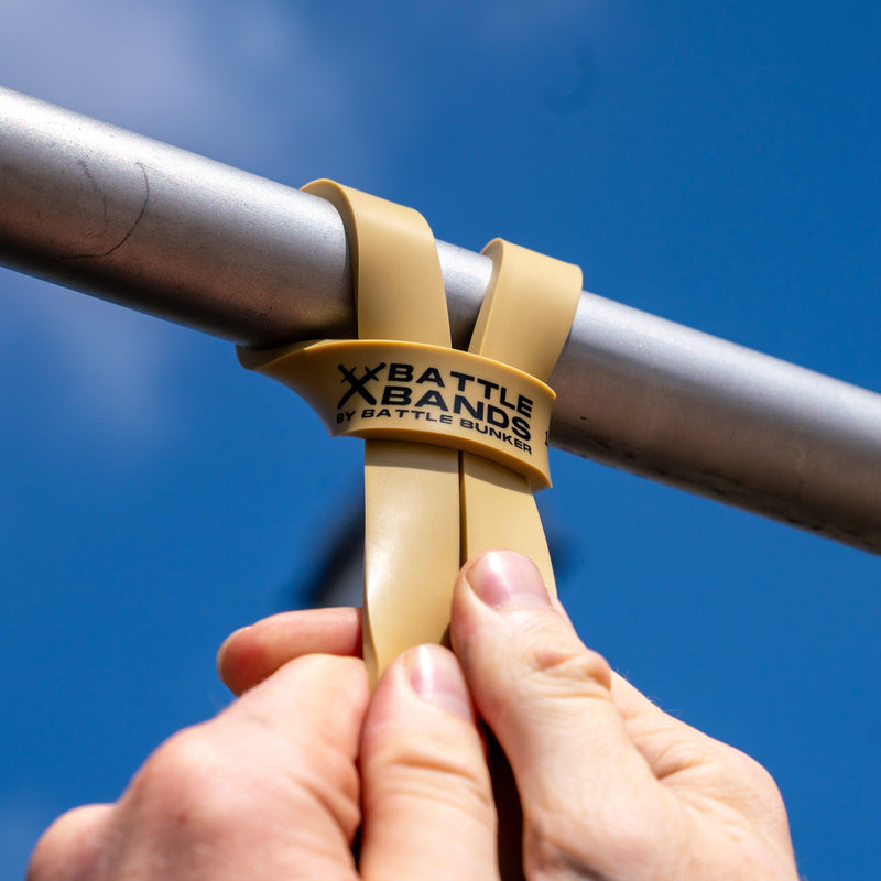 Hands attaching beige Battle Bands resistance strap by Battle Bunker to metal bar under blue sky