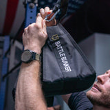 Man attaching black Battle Bunker strap with carabiner in gym setting, close-up hands and watch