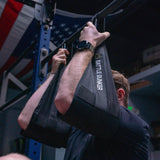 Person doing pull-up with black Battle Bunker arm slings in a gym with American flag background
