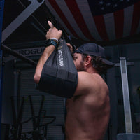 Muscular man doing pull-ups with Battle Bunker arm support in gym with American flag