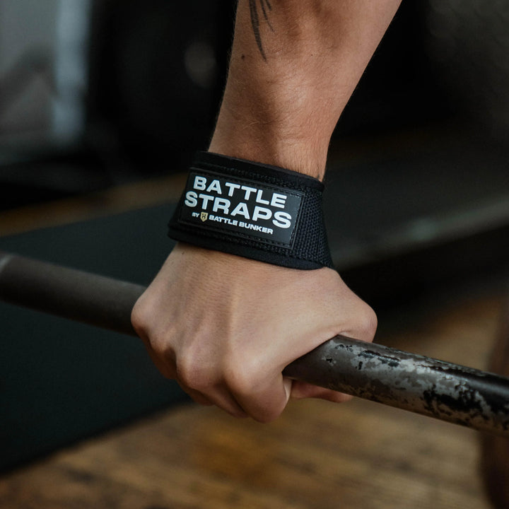 Hand gripping metal bar wearing black Battle Straps by Battle Bunker wrist support