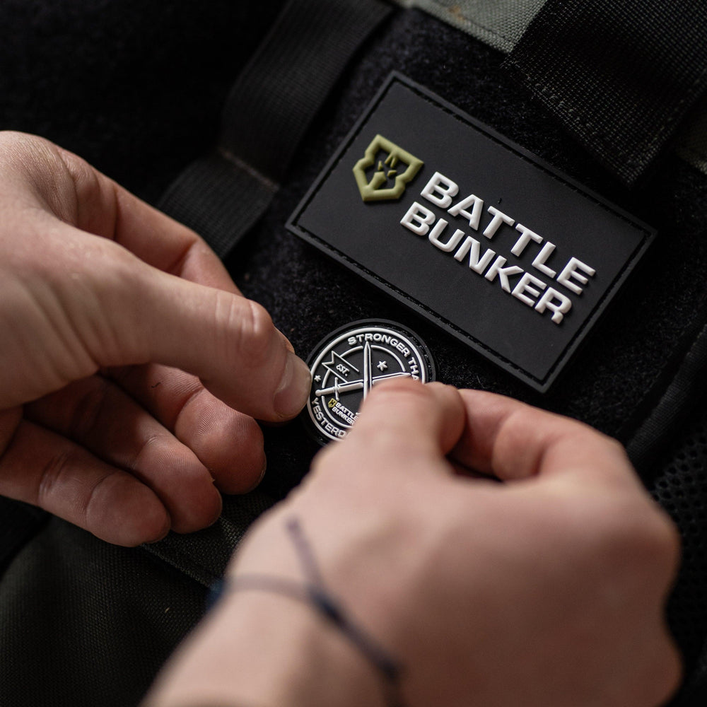 Hands attaching a Battle Bunker patch on black tactical gear with Battle Bunker logo