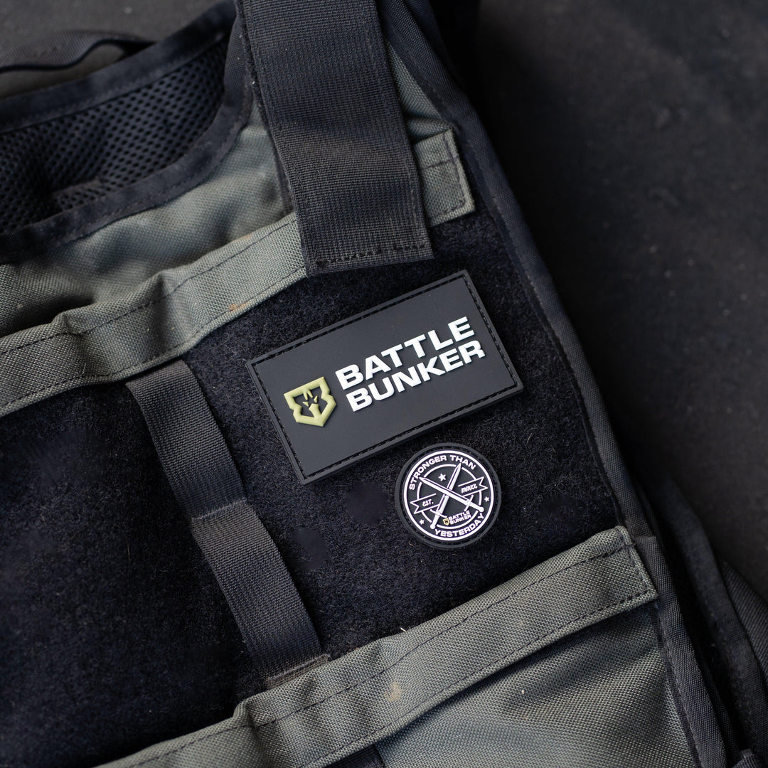 Close-up of a tactical vest with Battle Bunker logo patch and round badge on black and green fabric