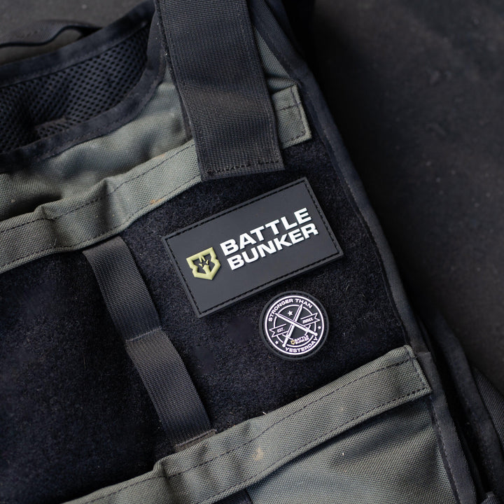 Close-up of a tactical vest with Battle Bunker logo patch and round badge on black and green fabric