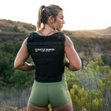 Woman outdoors wearing black Battle Bunker Hybrid Vest MK1, green shorts, standing in natural landscape