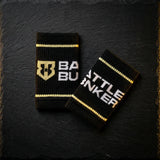 Black Battle Bunker wristbands with gold stripes and logo on dark textured background