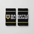 Black Battle Bunker sweat wristbands with gold stripes and white logo text on gray background