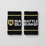 Black Battle Bunker sweat wristbands with gold stripes and white logo text on gray background