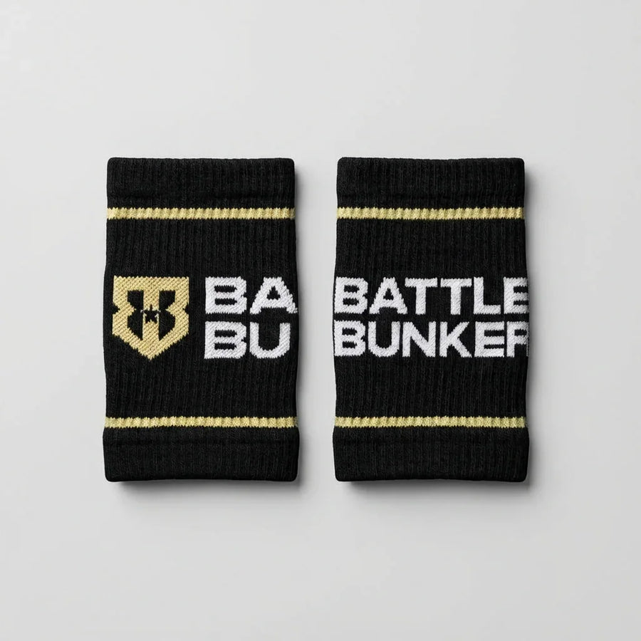 Black Battle Bunker sweat wristbands with gold stripes and white logo text on gray background