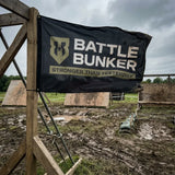 Battle Bunker black banner with logo and slogan at muddy outdoor obstacle course under cloudy sky