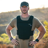 Man wearing black Battle Bunker tactical vest and cap outdoors in sunny rugged terrain