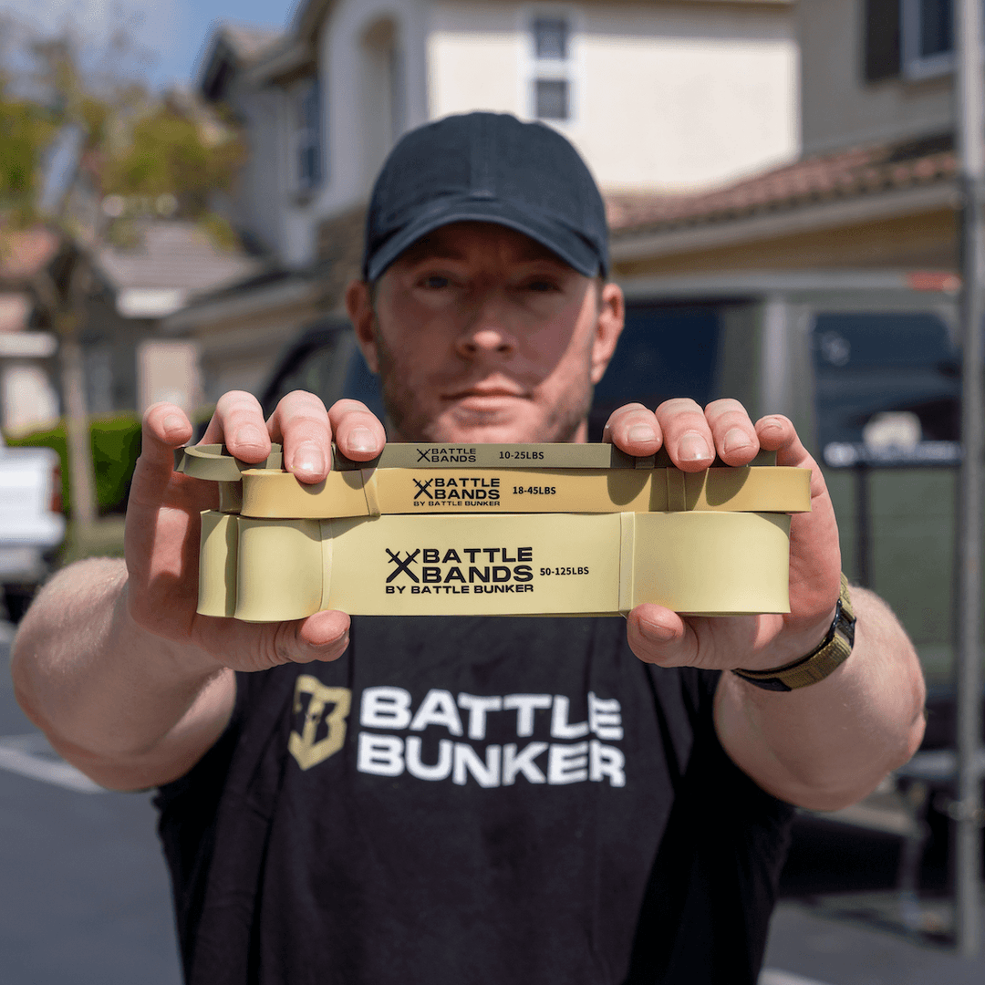 Man holding three beige Battle Bands resistance bands by Battle Bunker with different weight levels outdoors