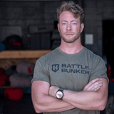muscular man with folded arms wearing a Battle Bunker t-shirt in an indoor gym setting