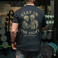 Man wearing black shirt with 'Stay in the Fight Battle Bunker Co.' and skeleton soldier graphic in gym