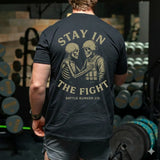 Man wearing black shirt with 'Stay in the Fight Battle Bunker Co.' and skeleton soldier graphic in gym