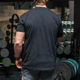 Man wearing black t-shirt in gym with dumbbells and weight plates, Battle Bunker fitness setting