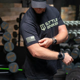 Man in gym wearing black Battle Bunker t-shirt with American flag on sleeve and smartwatch