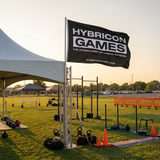 Outdoor fitness event setup with 'Hybricon Games' flag and exercise equipment.
